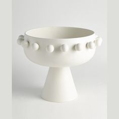 a white bowl that has balls on the rim and is sitting in front of a white background