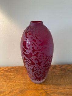 a red vase sitting on top of a wooden table next to a white walled wall