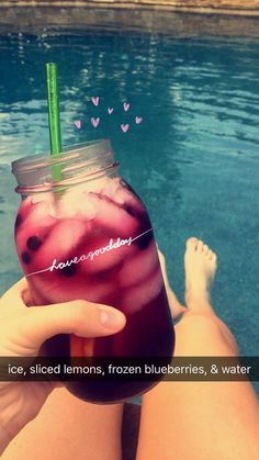 a person holding a drink in front of a body of water with hearts floating on it