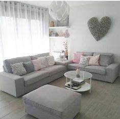 a living room with grey couches and pink pillows on the walls, coffee table