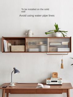 a wooden desk topped with a shelf filled with books next to a wall mounted plant