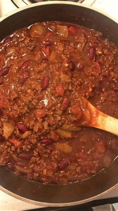 a pot filled with chili and potatoes on top of a stove next to a wooden spoon