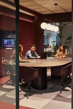 three people sitting at a round table in an office