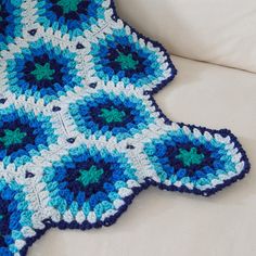 a blue and white crocheted afghan sitting on top of a couch next to a pillow