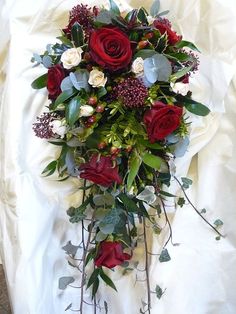 a bouquet of red roses and greenery on a white cloth covered bed sheet,