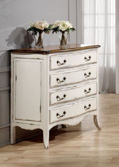 two vases with flowers sit on top of an old white dresser in a room