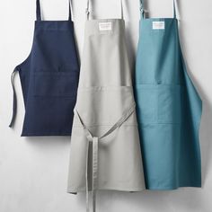 three aprons are hanging on the wall next to each other, and one is blue