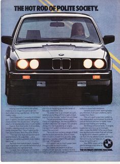 the front end of a black bmw car with its lights on, and an advertisement for the