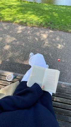 a person is reading a book on a park bench near the water and grass,