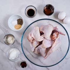 raw chicken in a glass bowl surrounded by ingredients for the recipe on a marble countertop