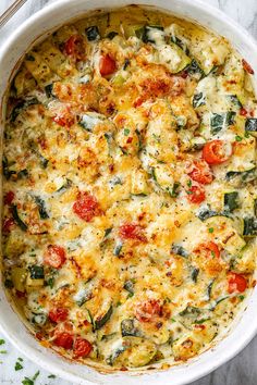 a casserole dish filled with cheese, tomatoes and spinach on a marble surface