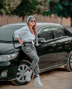 a woman standing next to a car in front of her wearing sunglasses and a beanie