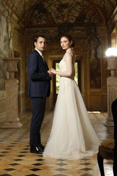 a bride and groom standing in an ornate hall holding hands with each other as they look into the distance