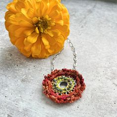 a yellow flower sitting on top of a cement floor next to a chain necklace with an open hole in the center