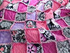 a pink and black quilt on top of a bed covered in purple and white fabric