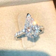 an engagement ring with a pear shaped diamond surrounded by small round brilliant cut diamonds in a box