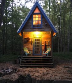 a small cabin in the woods with two chairs on the front porch and steps leading up to it