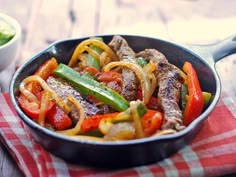 a skillet filled with meat, peppers and onions