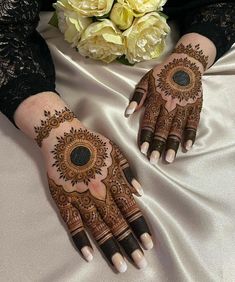 two hands with henna designs on them sitting next to a bouquet of white roses