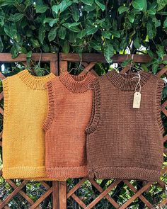 three sweaters hanging on a clothes line in front of a fence with green leaves