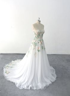 a white wedding dress with flowers on the bouncy skirt is displayed in front of a white wall