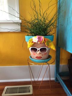 a potted plant with sun glasses on it sitting on a stand in front of a yellow wall