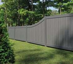 a large gray fence in the middle of a grassy area with trees and bushes around it