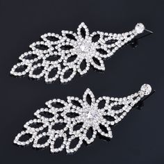 two pairs of white crystal earrings on a black background, one has a flower design and the other is a leaf shape