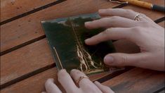 two hands on a wooden table with a notebook and pen in front of the person's hand