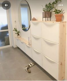 a white dresser sitting next to a mirror and potted plant