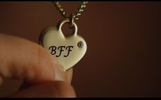 a person holding a heart shaped necklace with the letter bff on it's side