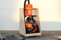 an orange and black vacuum sitting on top of a wooden stand next to a garage door