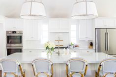 a large kitchen with white cabinets and marble counter tops, along with four chairs at the center island