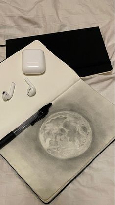 an apple airpods sitting on top of a notebook with the moon drawn on it