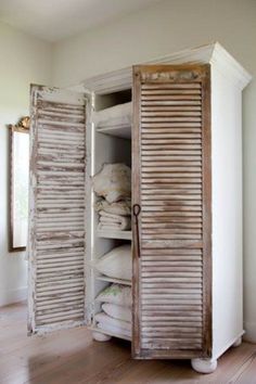 an open shuttered closet in the corner of a room with wood floors and white walls