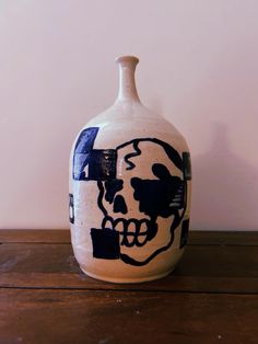 a white and black vase with a skull painted on it's side sitting on a wooden table