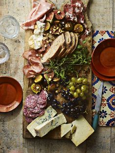 an assortment of meats and cheeses on a cutting board with wine glasses next to it