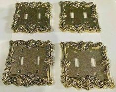 four antique brass plated switchplate covers with ornate designs on each one and two toggles