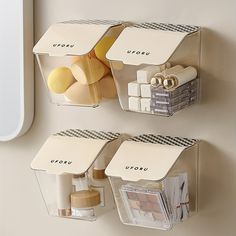 two clear storage containers on the wall with makeup and toiletries in each bins