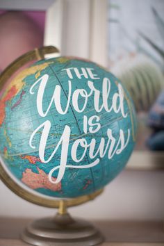 a globe with the words the world is yours written on it, in front of a photo