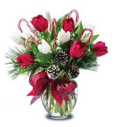 a glass vase filled with red and white flowers, candy canes and greenery