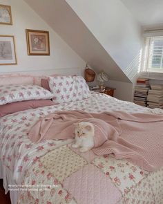 a white cat laying on top of a bed covered in pink and white blankets next to a window