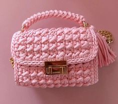 pink crocheted purse with gold hardware and tassels on the handle, against a pink background