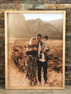 a man and woman standing in front of a stone wall holding a small child with mountains in the background