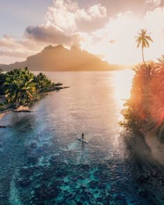 a person on a surfboard in the water near an island with palm trees and mountains