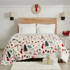 a christmas themed bed in a bedroom with white walls and wood flooring, decorated for the holidays