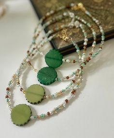 three necklaces with green and white beads on top of a table next to a book