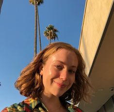 a woman standing in front of a palm tree with her hair blowing in the wind