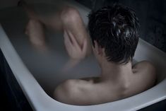 a man is sitting in the bathtub with his back turned to the camera,