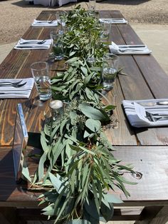 a long wooden table with place settings and greenery on the top, along with silverware